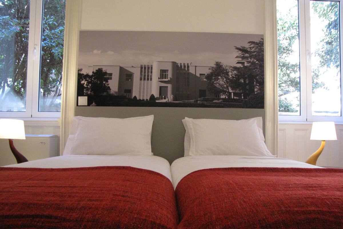 A hotel room with a bed, two bedside lamps, and a large window.