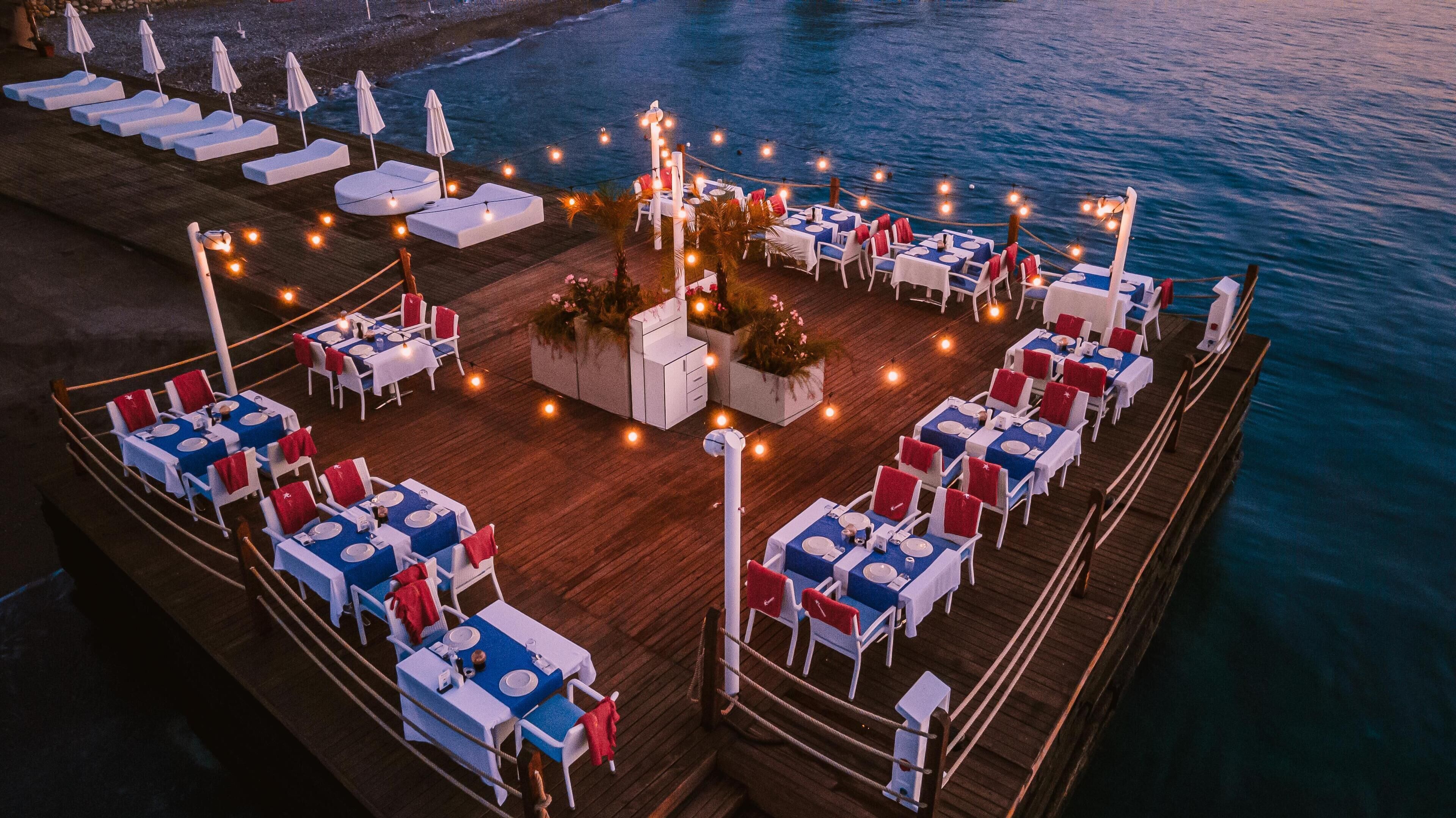 A deck with tables and chairs, a pool area, and a view of the ocean.