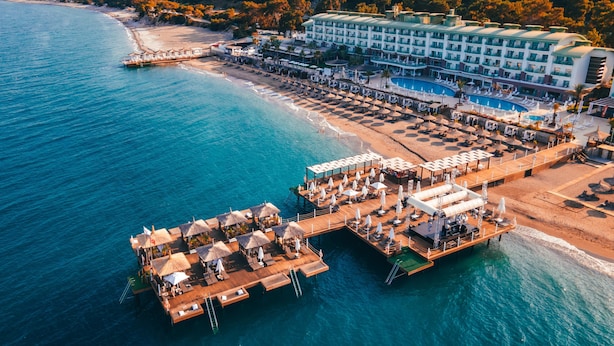 Vista aérea de un complejo turístico costero con un hotel grande, una playa y bungalós sobre el agua.