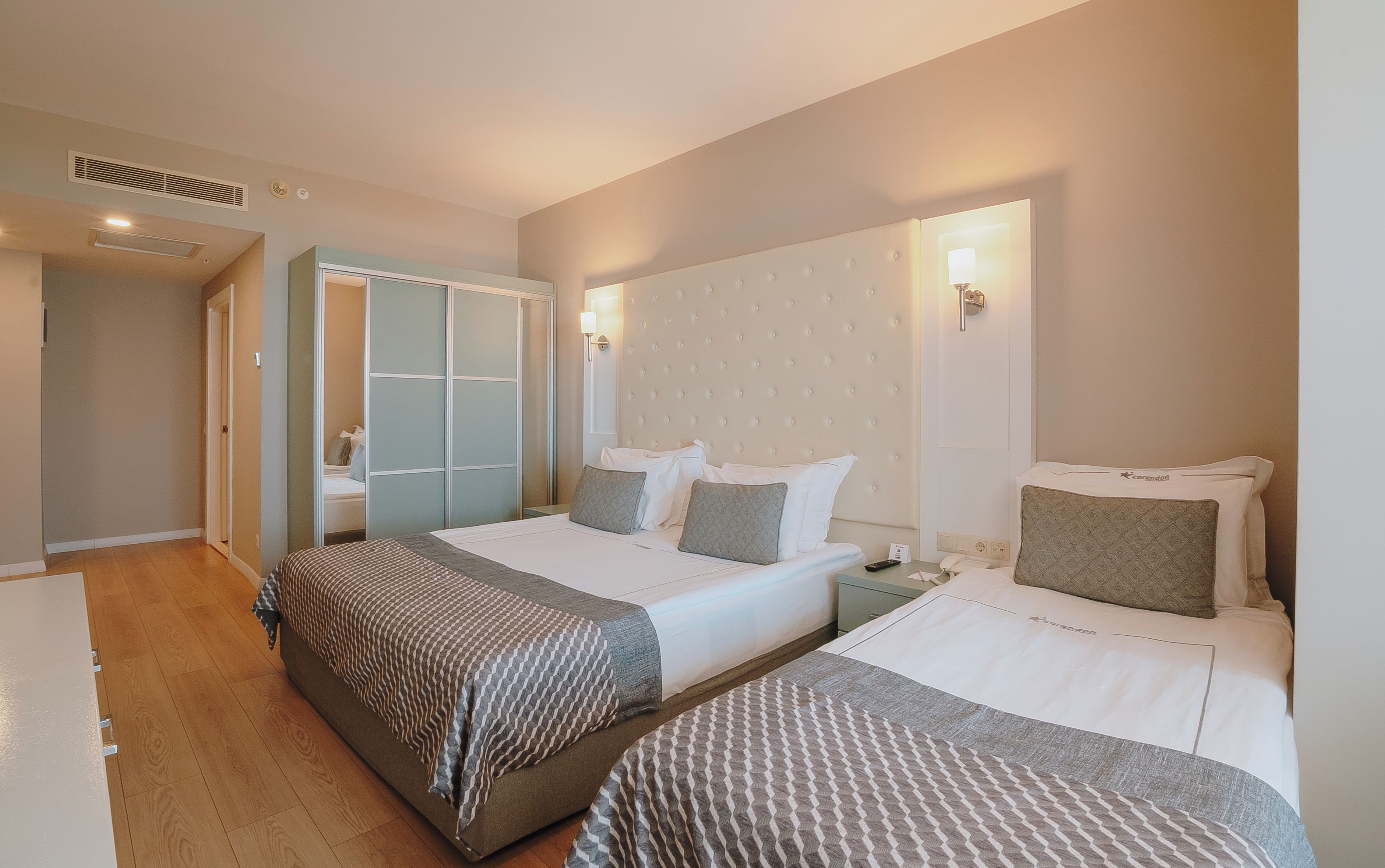 A hotel room with two beds, a wardrobe, and a bedside table.