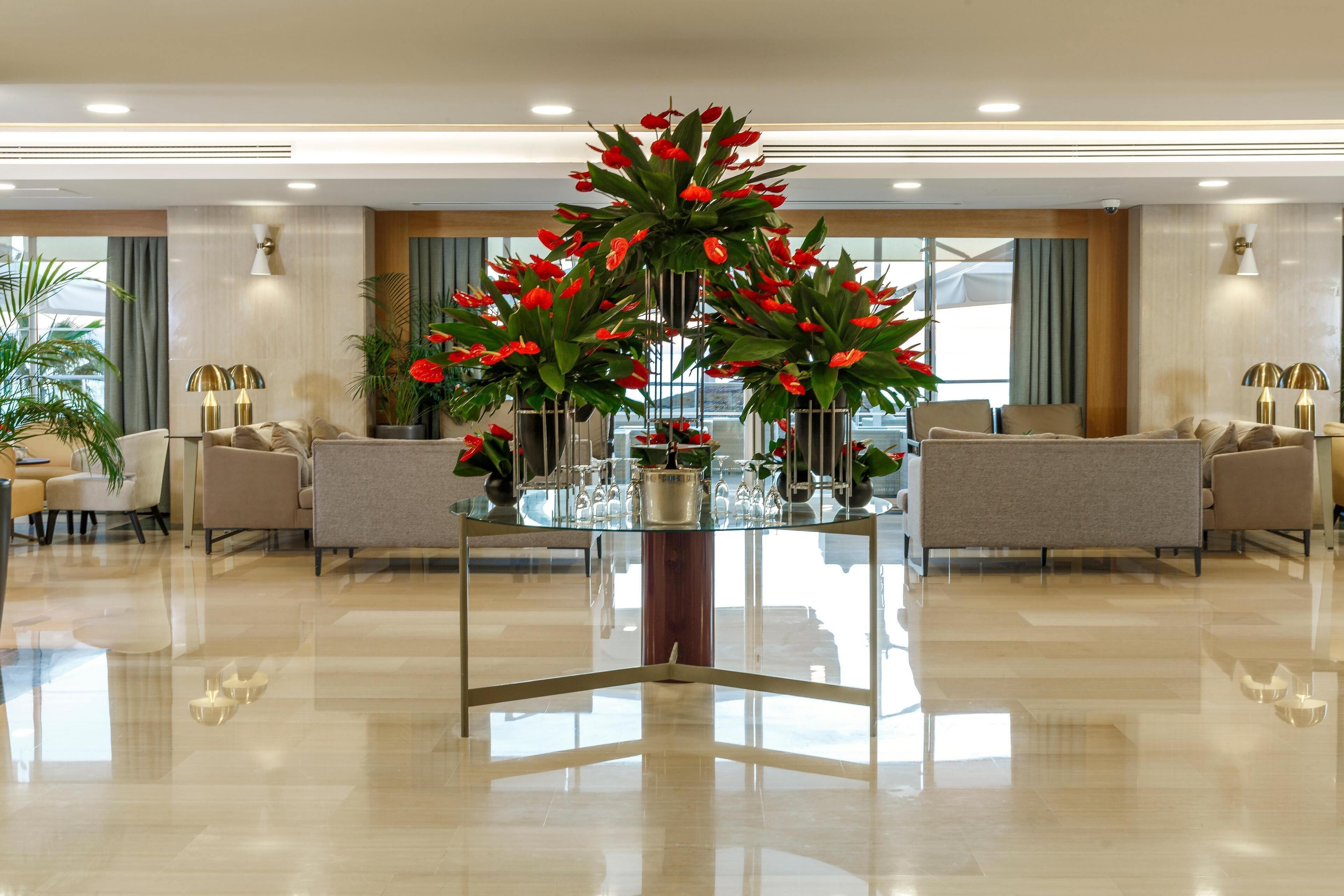 A modern hotel lobby with a glass-top table, seating area, and large windows.