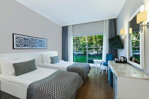 Habitación de hotel con dos camas, televisión, una mesita y vistas al exterior.