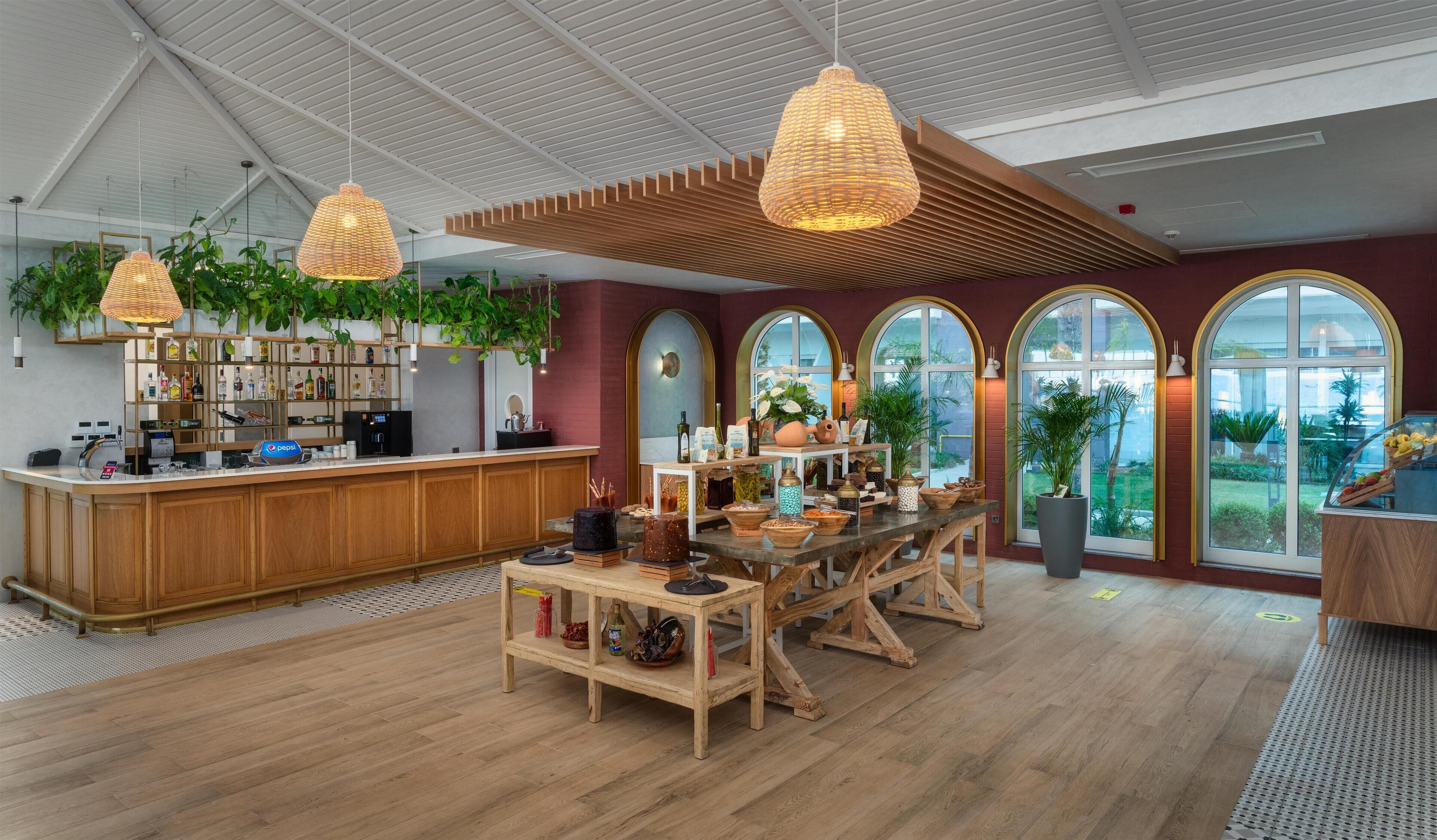 A modern bar area with wooden furniture, hanging wicker lights, and large arched windows offering views of the outdoors.