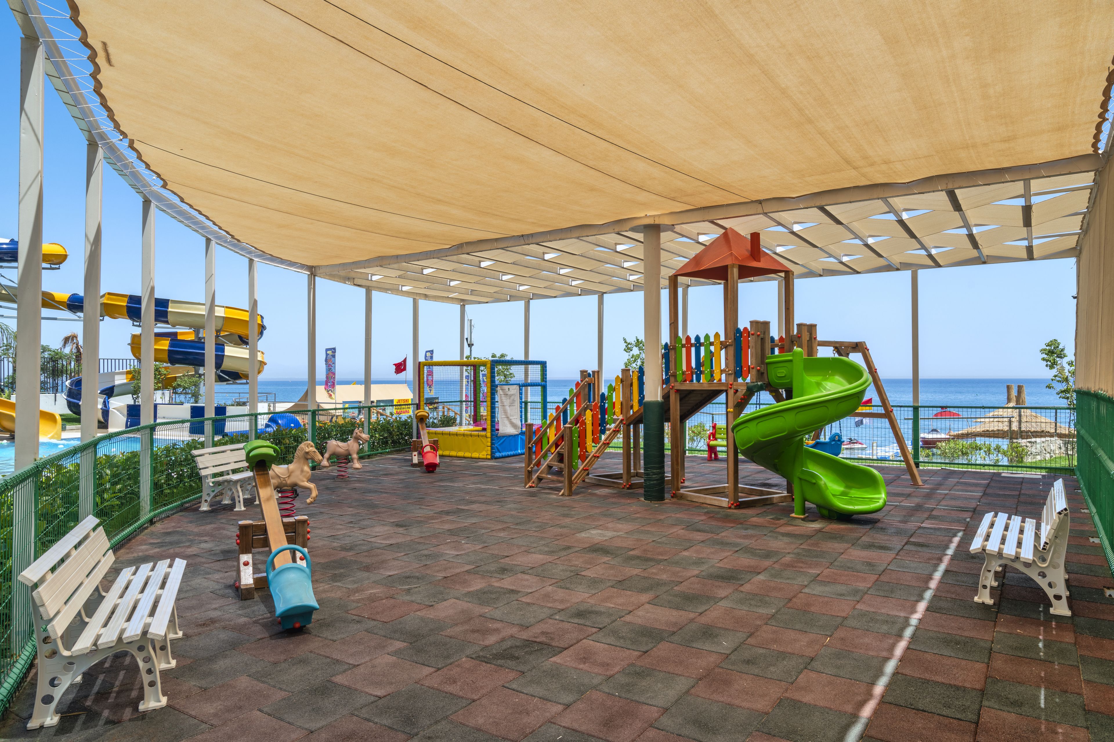 Un parque infantil techado con toboganes y columpios, con vista a una playa.