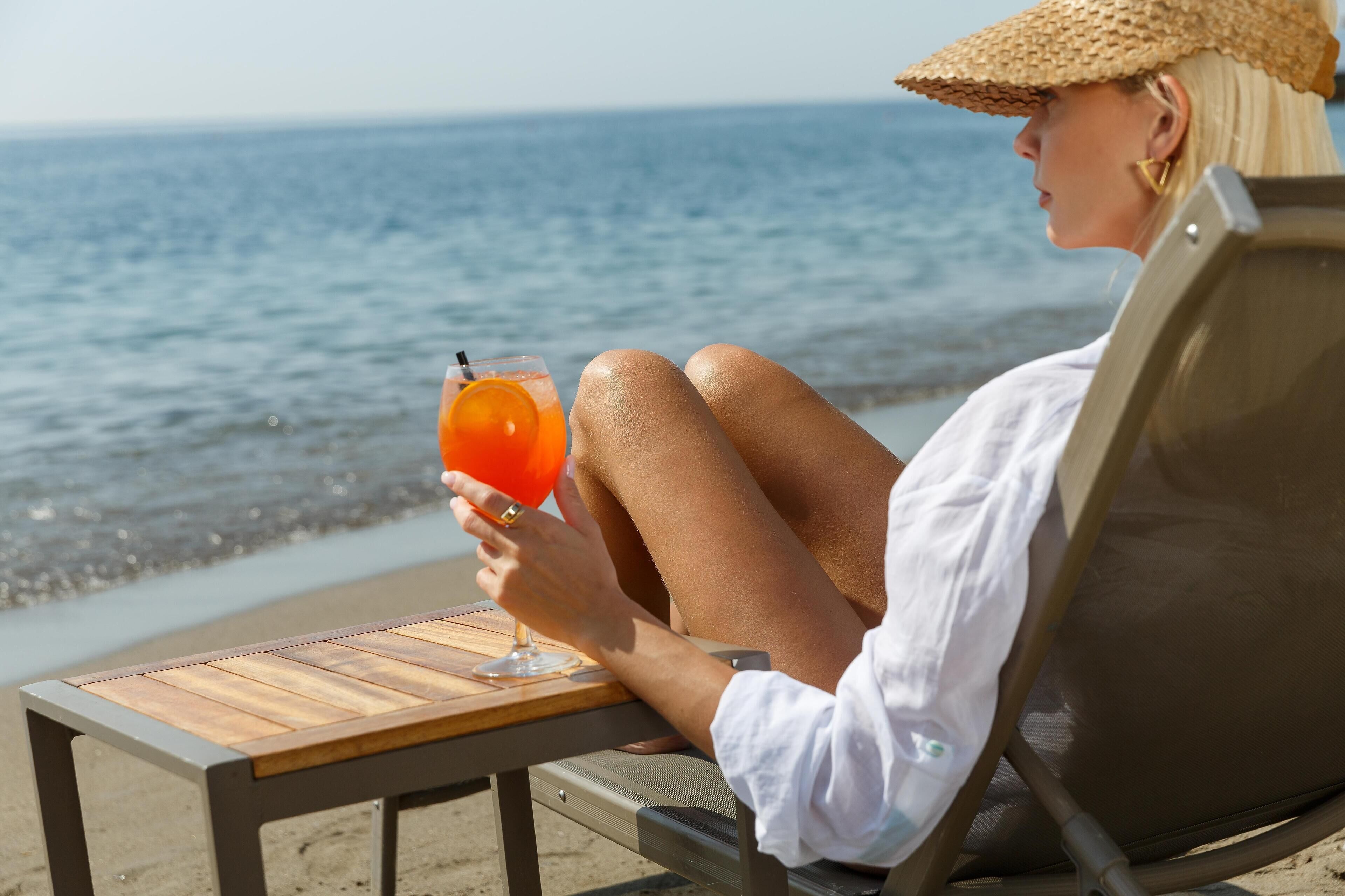 Une personne assise sur une chaise de plage, avec une boisson sur une table en bois.