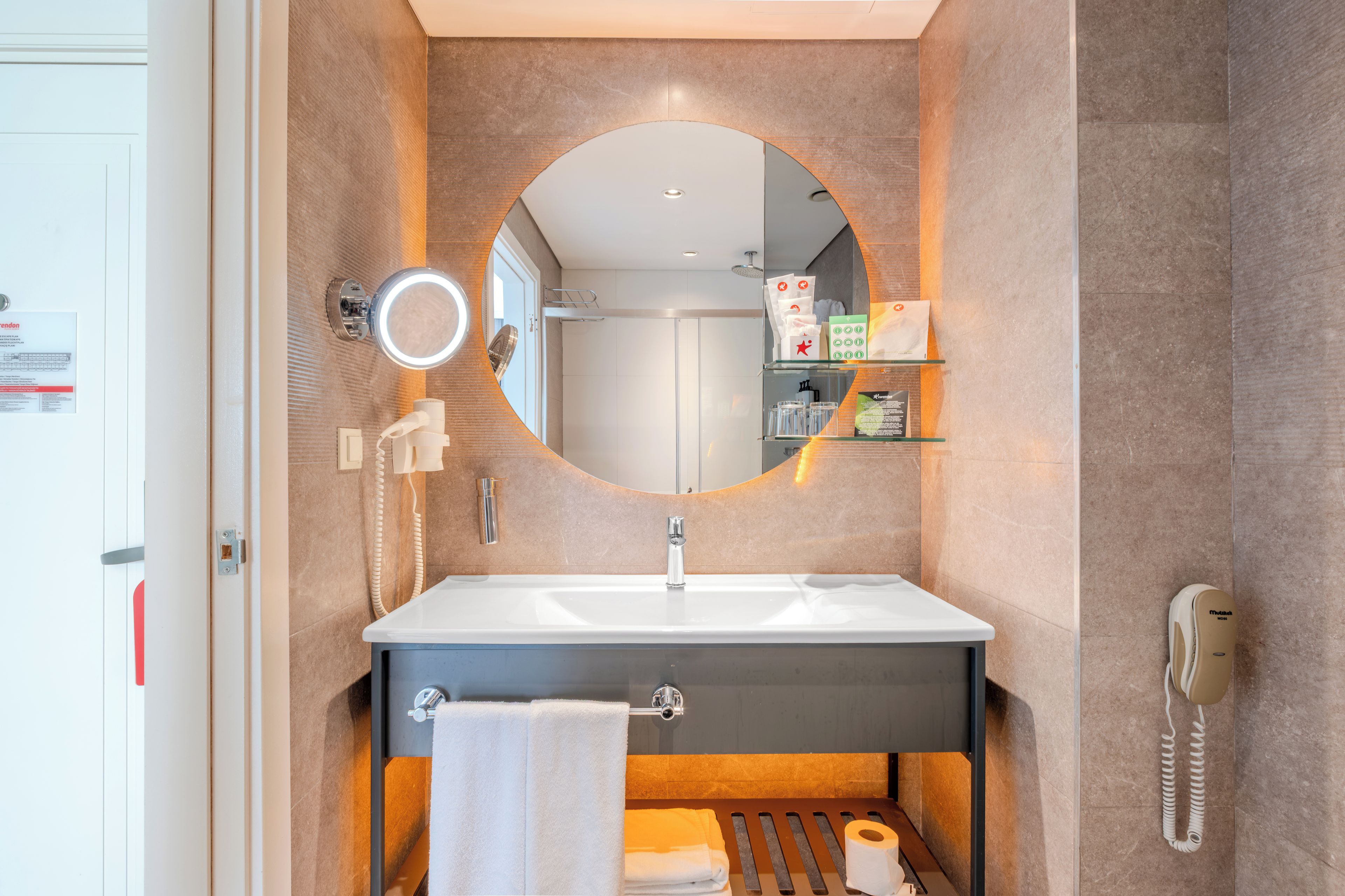A modern bathroom with a round mirror, a sink, a towel rack, and a toilet paper holder.