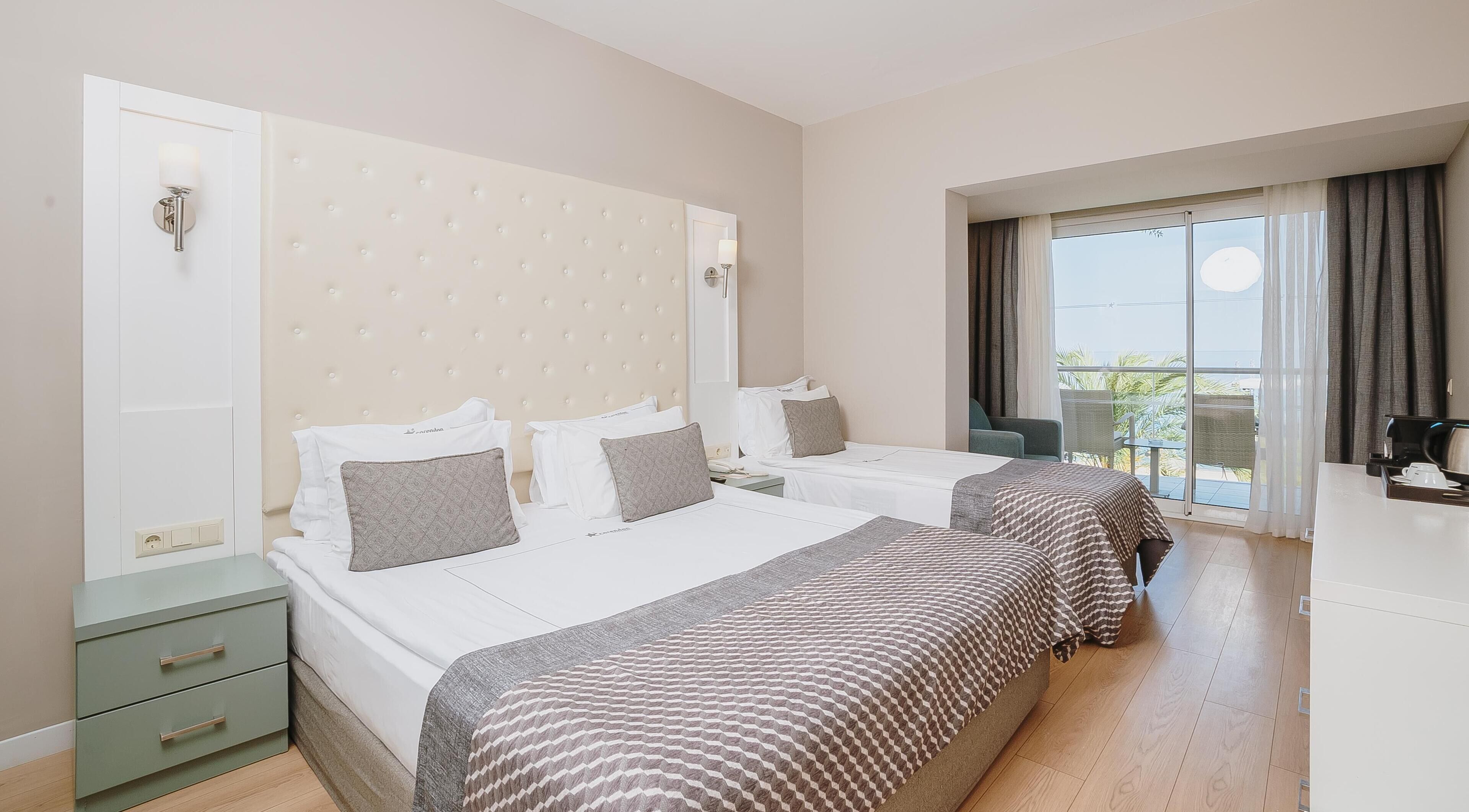 Habitación de hotel con dos camas, un balcón con cortinas y vistas al exterior.