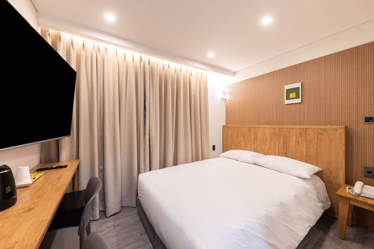 A hotel room with a bed, a desk with a chair, a TV, and a telephone.