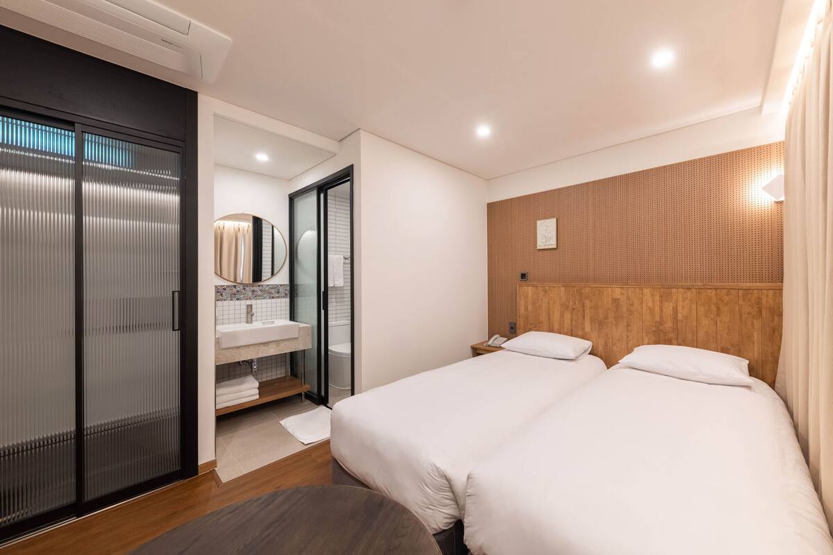 A hotel room with two beds, a bathroom with a shower, and a wooden headboard.