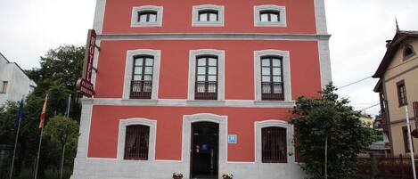 Un edificio de dos plantas con fachada roja y detalles blancos, que presenta una entrada central con escalones y plantas en macetas.