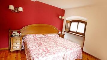 A bedroom with a wooden bed, a nightstand with a lamp, and a window with curtains.