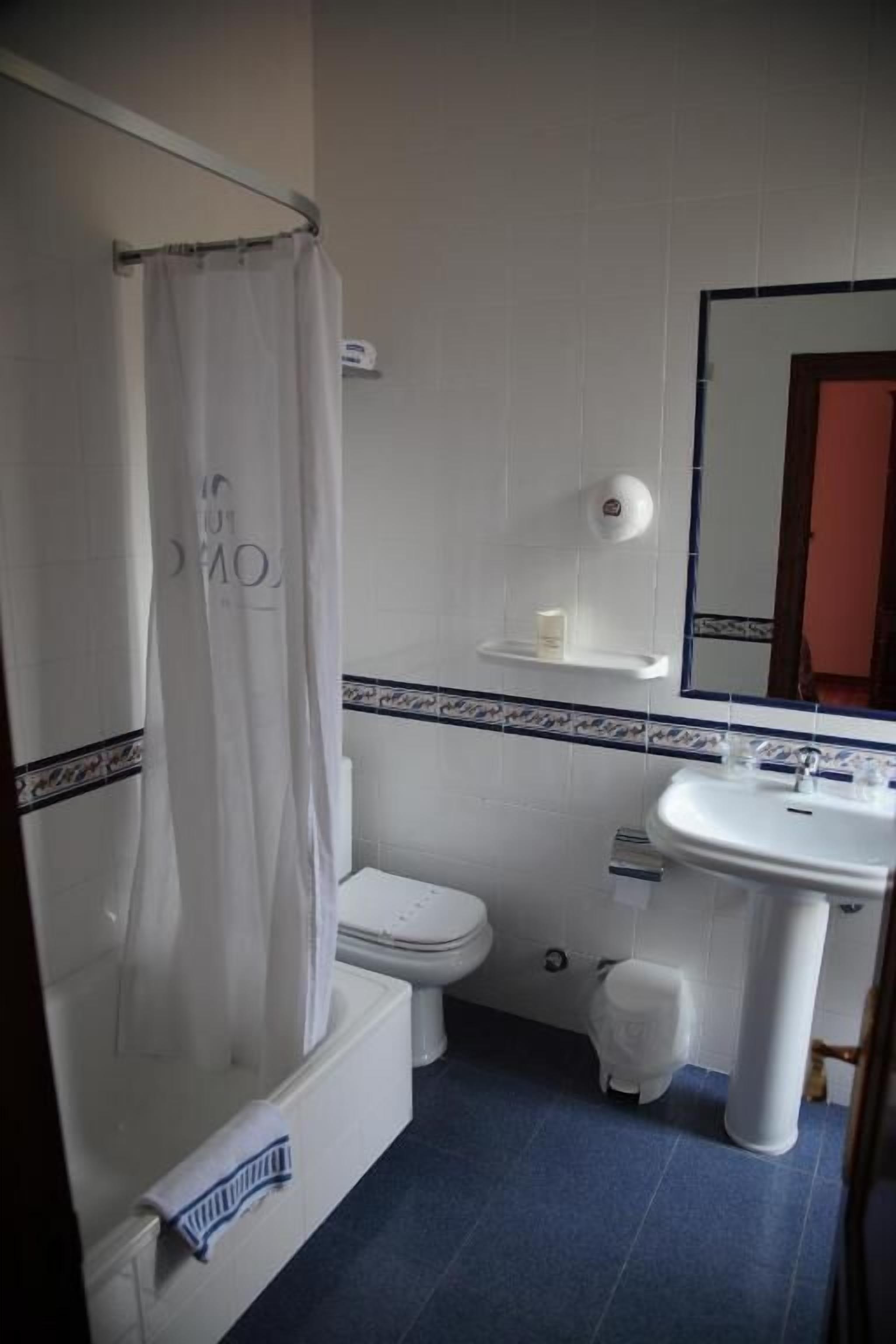 A bathroom with a shower curtain, toilet, sink, and mirror.