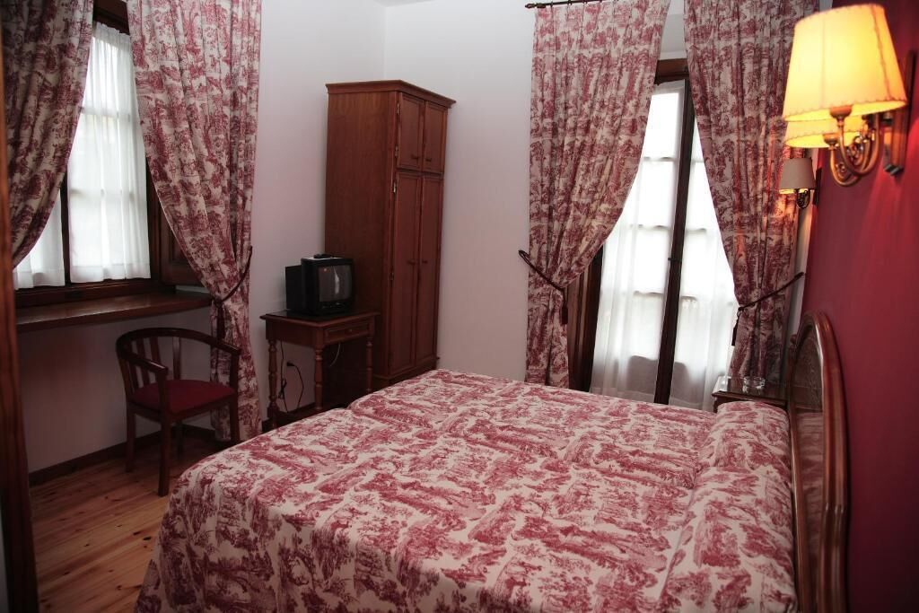 Um quarto com uma cama, um guarda-roupa de madeira, uma mesa de trabalho com uma televisão e uma cadeira.