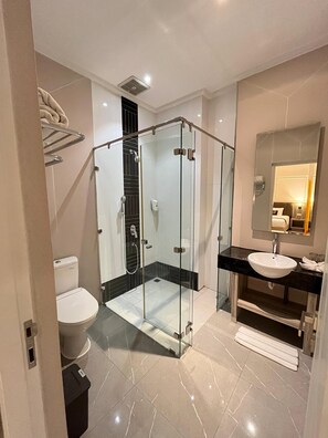 Une salle de bain moderne avec une douche à parois de verre, des toilettes blanches et un lavabo sur un plan de toilette noir.