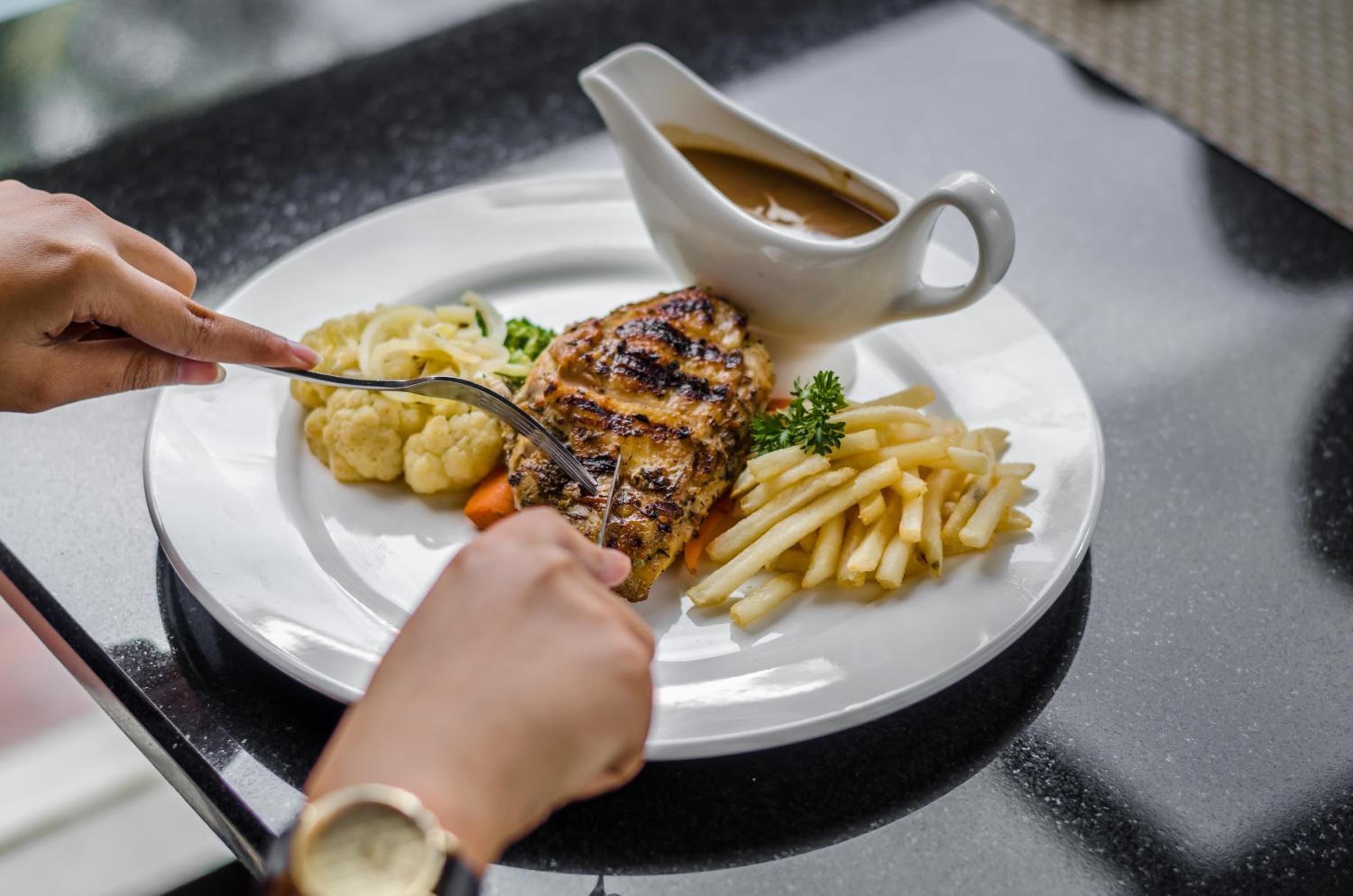 Une assiette composée de viande grillée, de purée de pommes de terre et de frites, accompagnée d’une sauce.