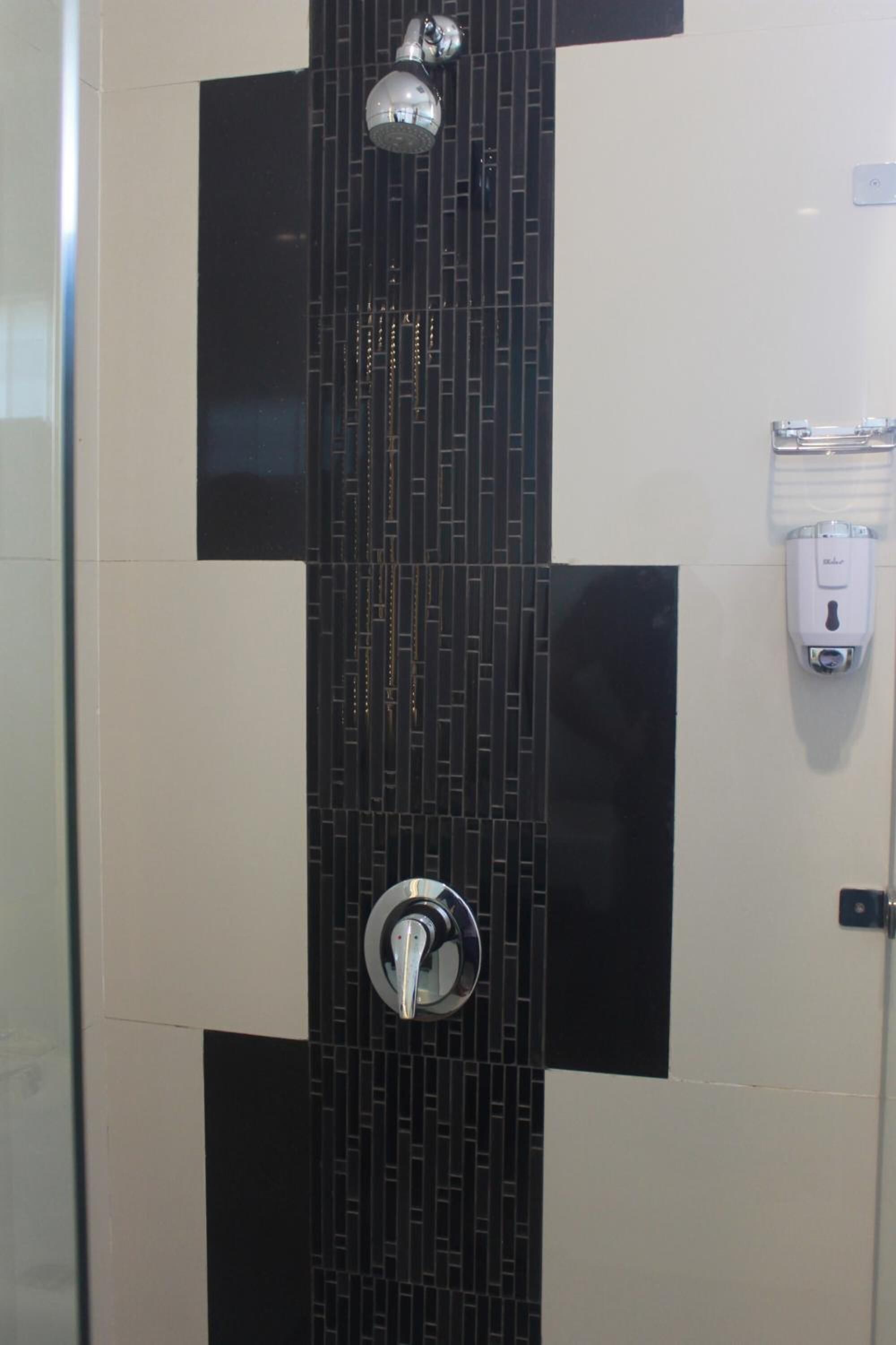 Ducha con un patrón vertical de azulejos blancos y negros, cabezal de ducha de mano y dispensador de jabón en la pared.