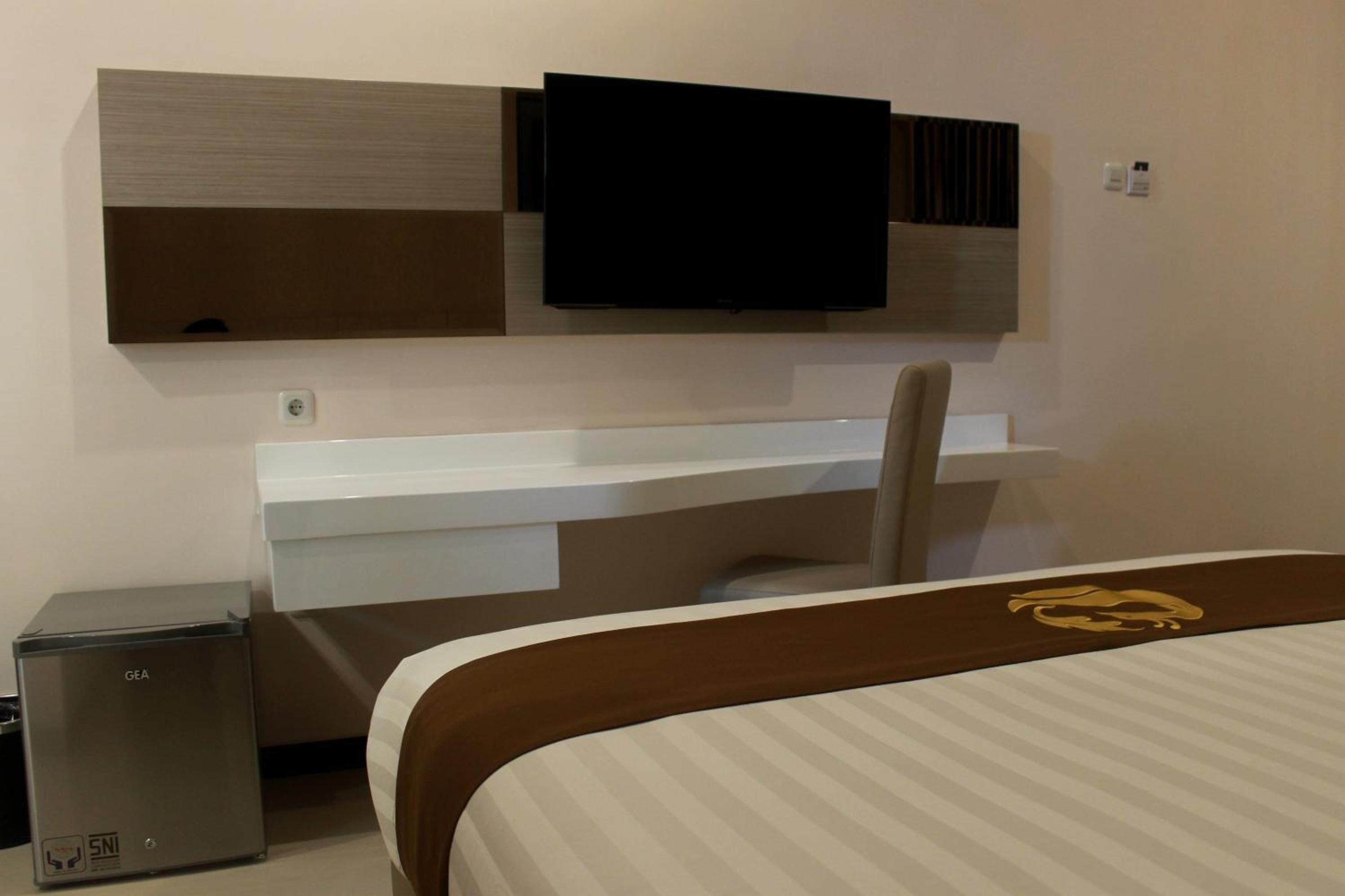 A hotel room with a bed, a desk, a chair, a television mounted on the wall, and a minibar.