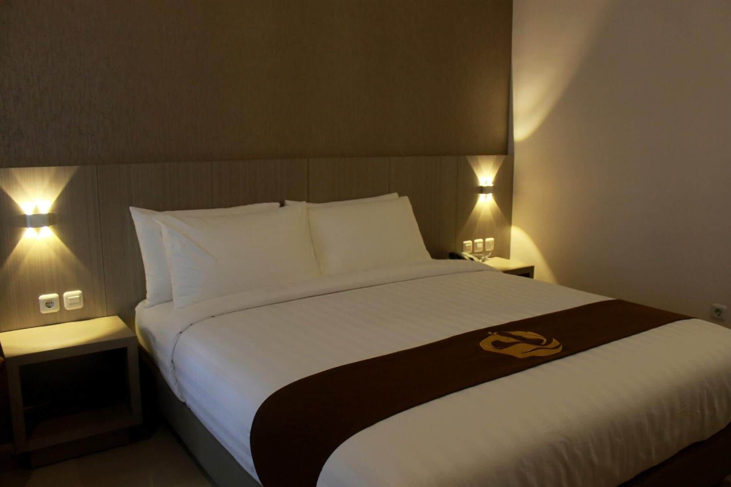 A hotel room with a neatly made bed, two bedside lamps, and a brown decorative item on the bed.