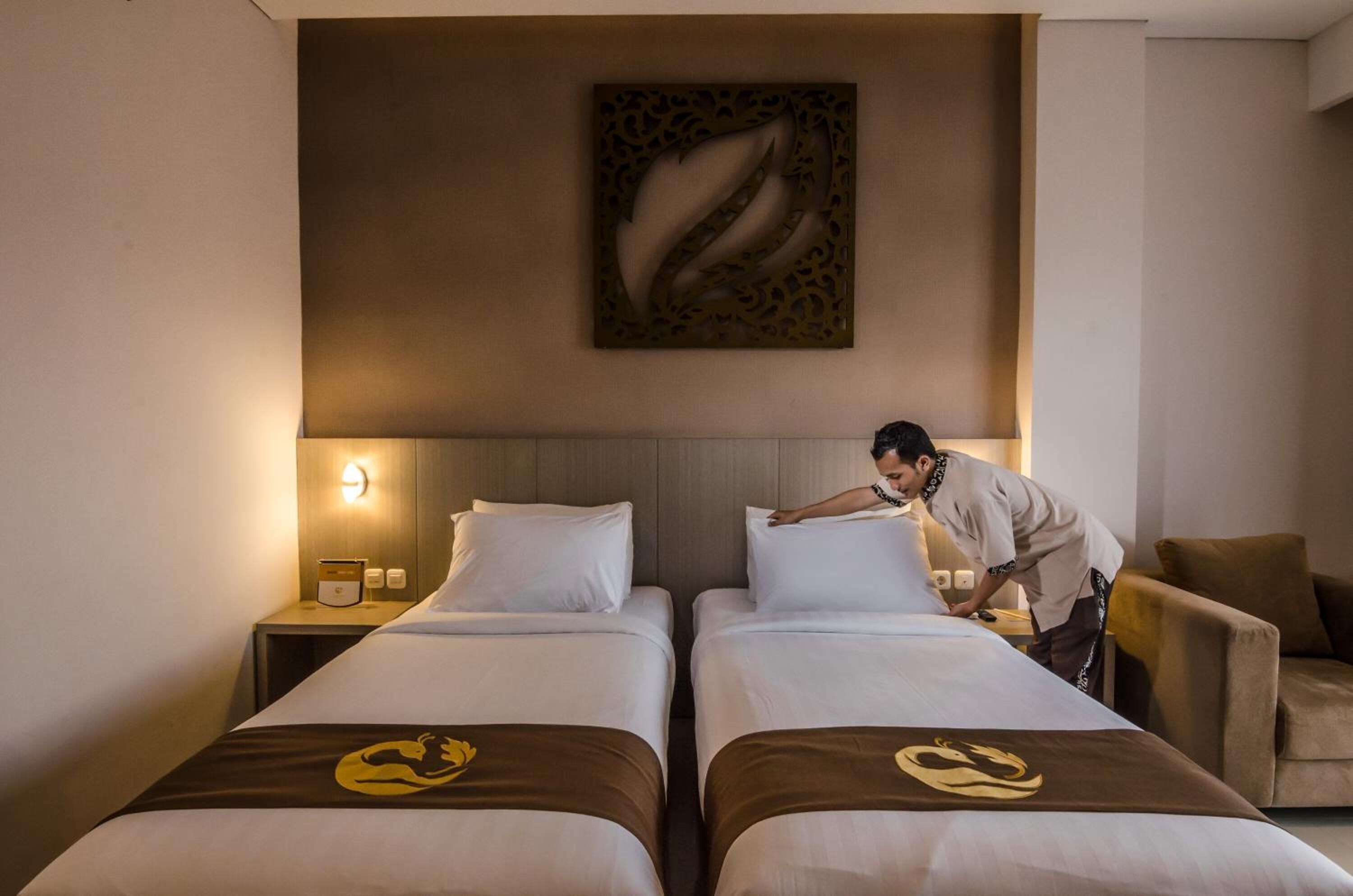 Habitación de hotel con dos camas, una mesita de noche con lámpara, una obra de arte en la pared y una silla.