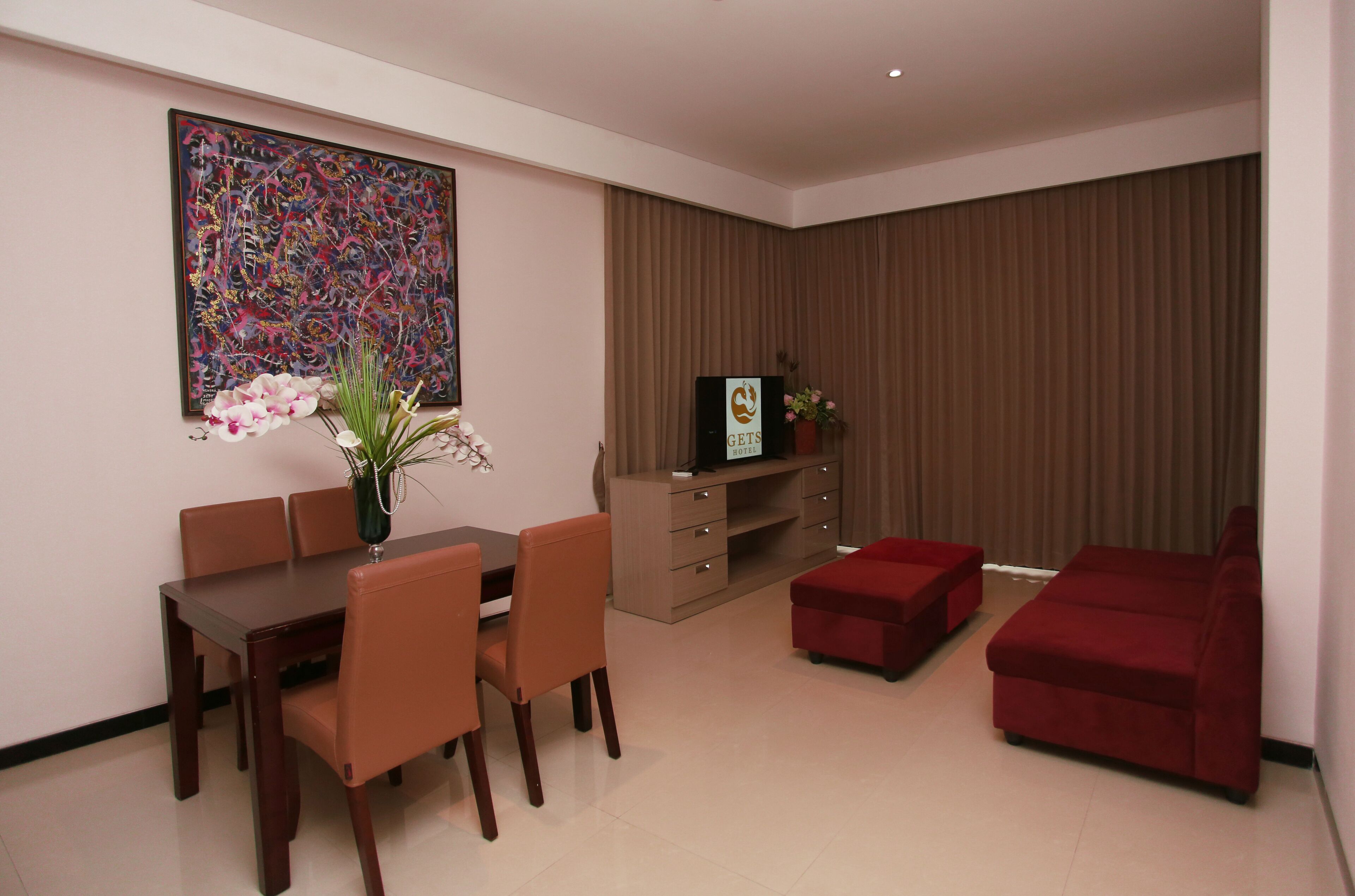 A modern living room with a dining area, a red sofa, a TV on a wooden cabinet, and a large abstract painting on the wall.