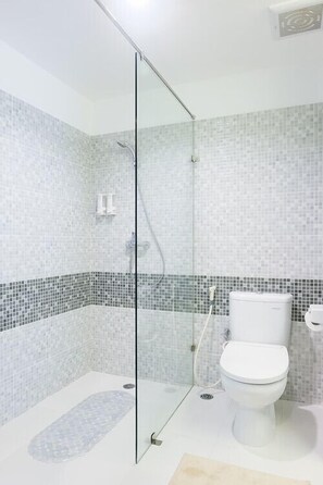 Un baño con cabina de ducha de vidrio, inodoro y suelo de baldosas.