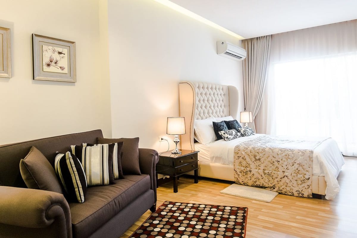 Habitación de hotel con cama, sofá, mesita de noche y aire acondicionado instalado en la pared.