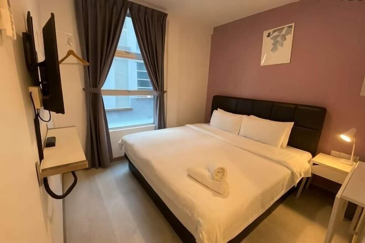 A hotel room with a bed, a bedside table, a TV mounted on the wall, a window with curtains, and a wall-mounted artwork.
