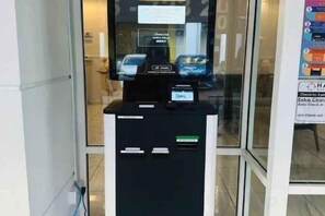 Un terminal en libre-service doté d’un écran numérique et d’un lecteur de cartes, situé dans une zone commerciale avec des portes vitrées.