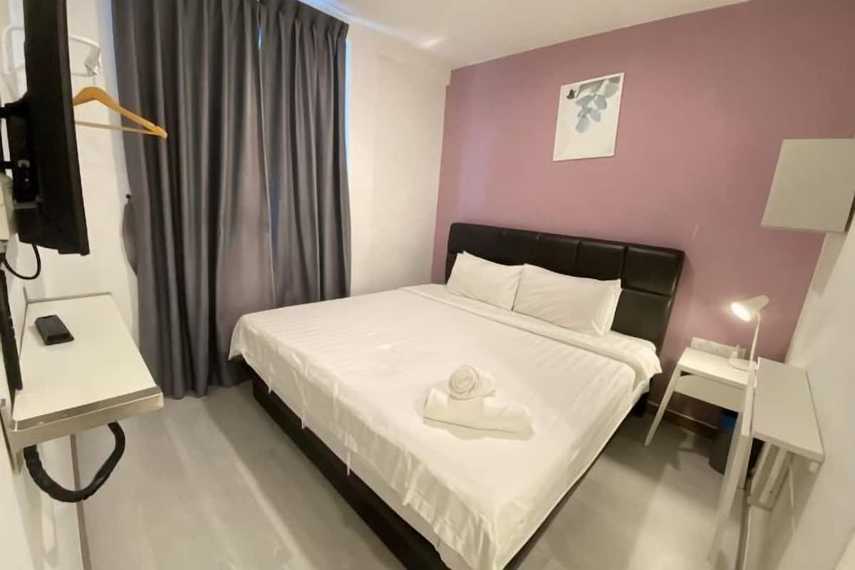 A hotel room with a bed, a bedside table, a lamp, a hanging coat rack, and a wall-mounted TV.