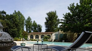 Un espace aménagé au bord de la piscine, avec des chaises longues, une petite table et une structure décorative en pierre.