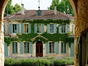 Een historisch gebouw met een gevel van natuursteen, groene luiken en een tuin met lavendel.