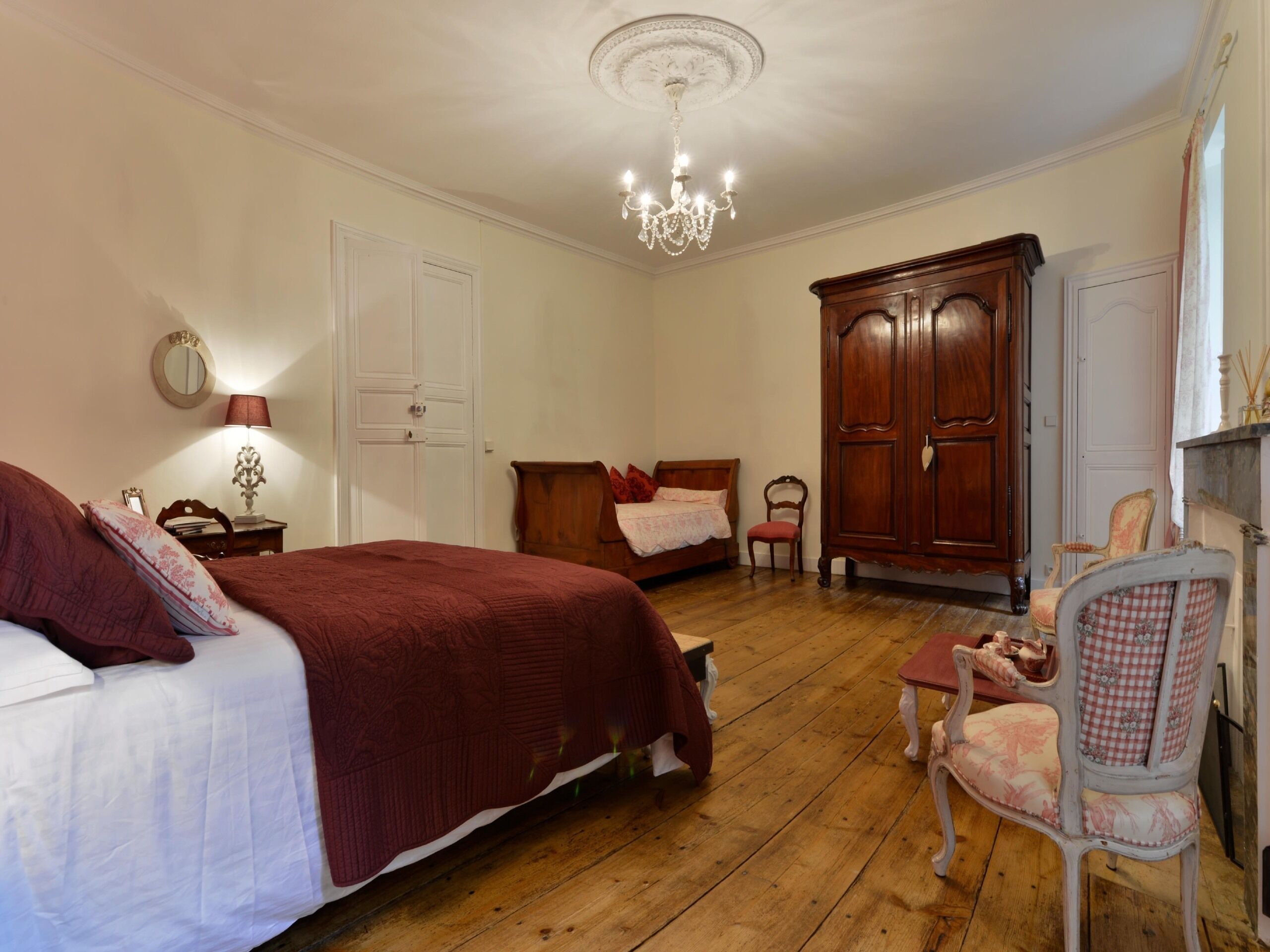 Een slaapkamer met een groot bed, een houten garderobe, een stoel en een kroonluchter.