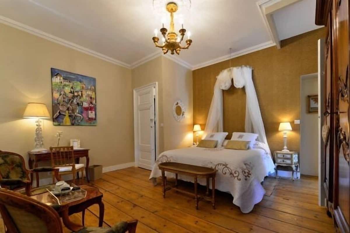 Ein Schlafzimmer mit Baldachinbett, Schreibtisch mit Stuhl, einem Wandbild und einer Chandelieber.