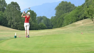 A golf course with a player in a red shirt and white shorts preparing to hit a ball.