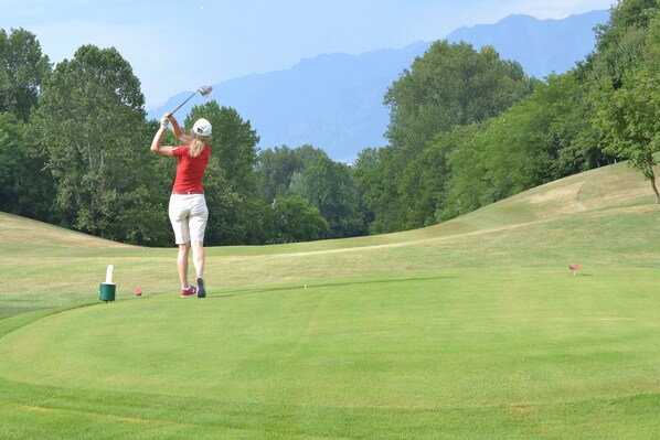 Un campo de golf con un jugador de camisa roja y pantalones cortos blancos preparándose para golpear la bola.