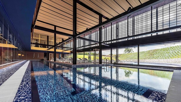 A modern indoor swimming pool with clear glass walls, a tiled floor, and a view of a vineyard outside. - Villaverde Hotel & Resort - Wellness Spa & Golf (Fagagna)