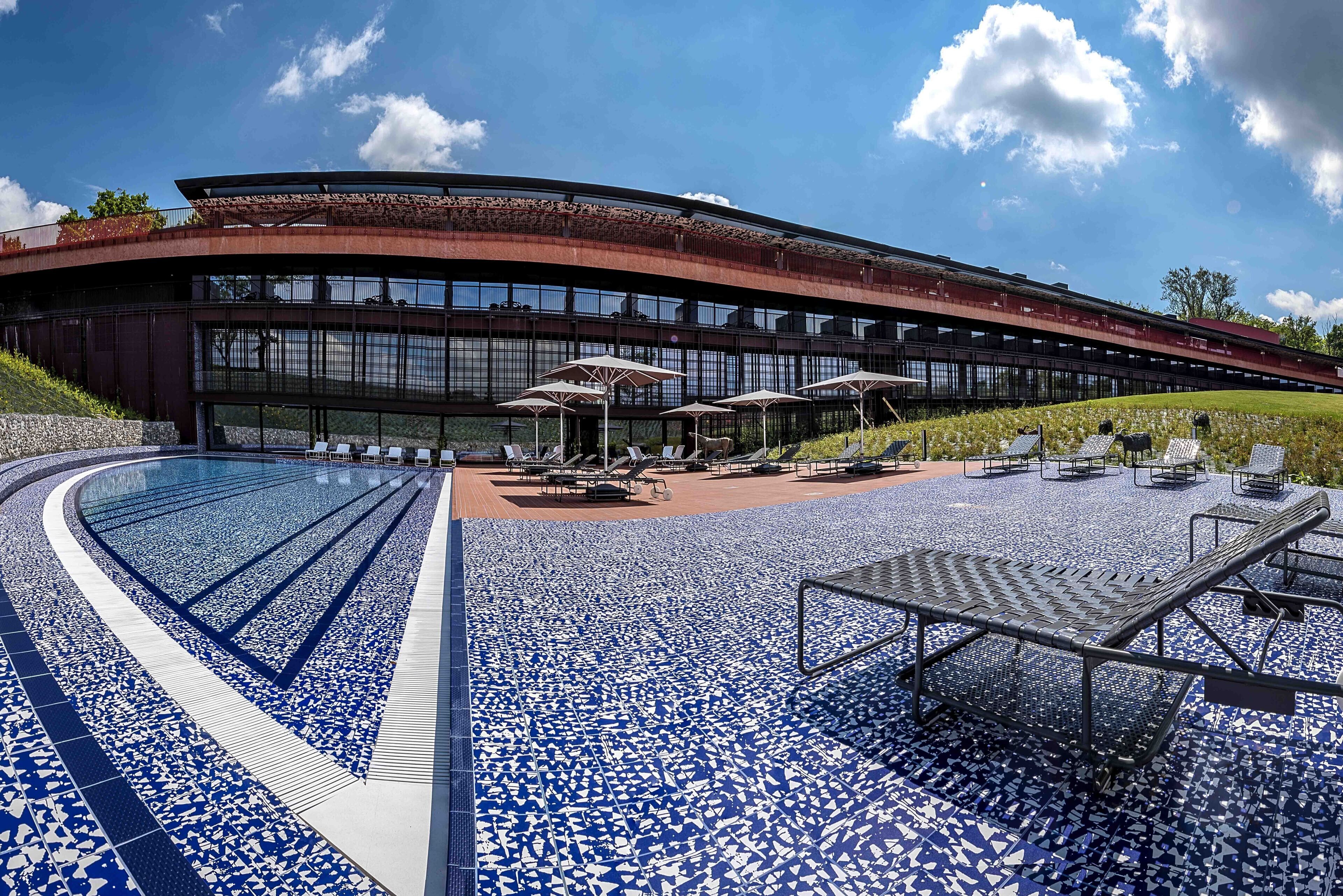 Edifici modern amb teulada corbada i zona de piscina amb gandules i ombrel·les.