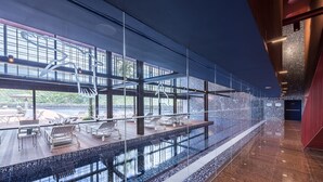 A modern indoor pool area with glass walls, lounge chairs, and a tiled floor. - Villaverde Hotel & Resort - Wellness Spa & Golf (Fagagna)