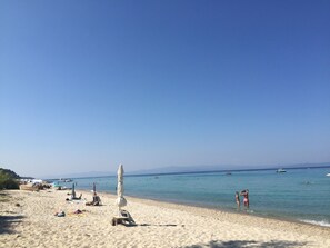 Una playa con cielos despejados, aguas tranquilas y varios barcos.