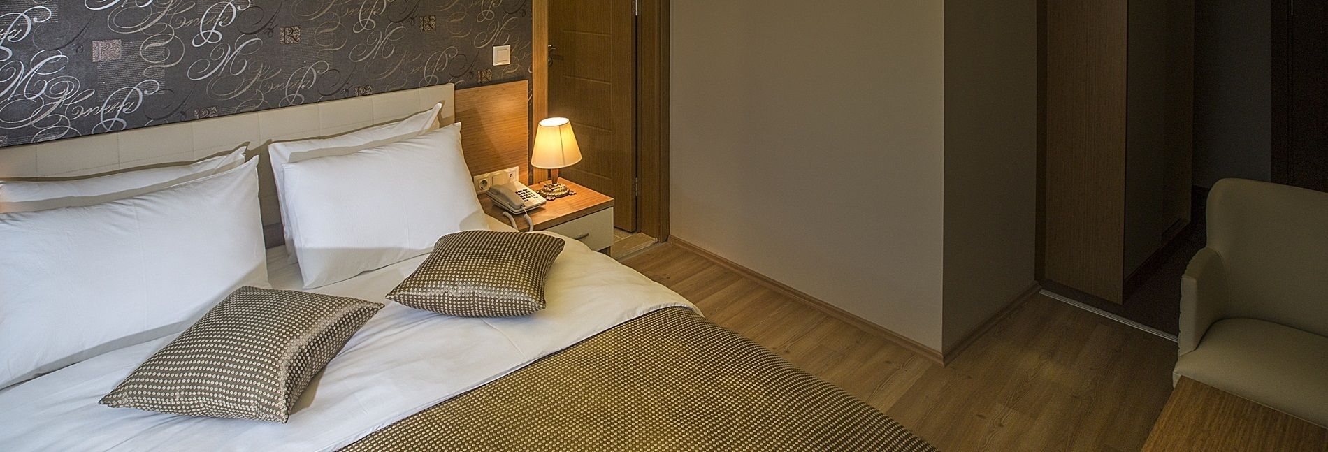 Una camera d'albergo con un letto, cuscini, un comodino con una lampada e una sedia.