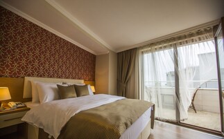 Habitación de hotel con una cama grande, una mesita de noche con lámpara, un papel tapiz estampado y un balcón con vistas.