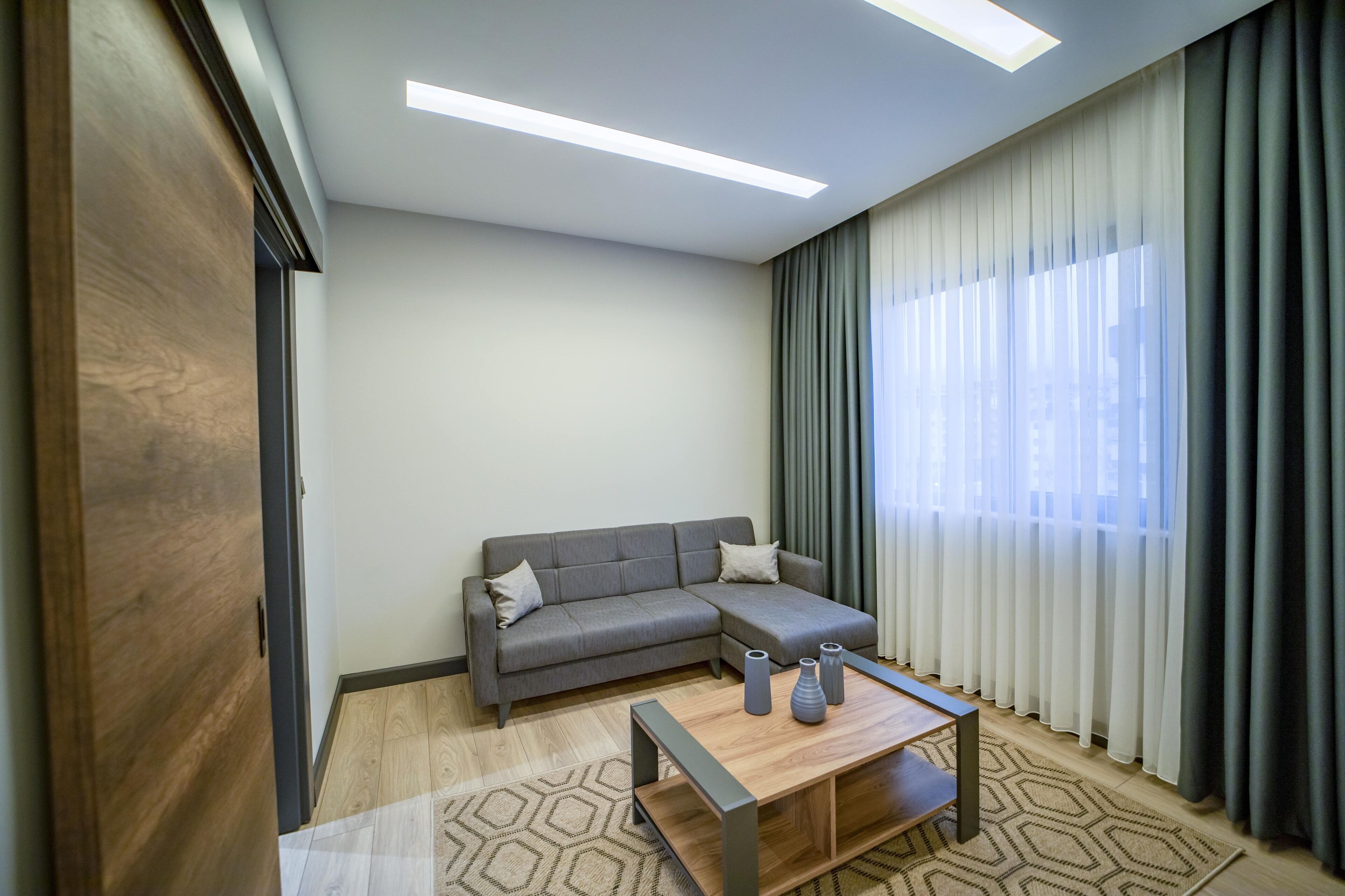 A modern living room with a grey sofa, a wooden coffee table, and sheer curtains.