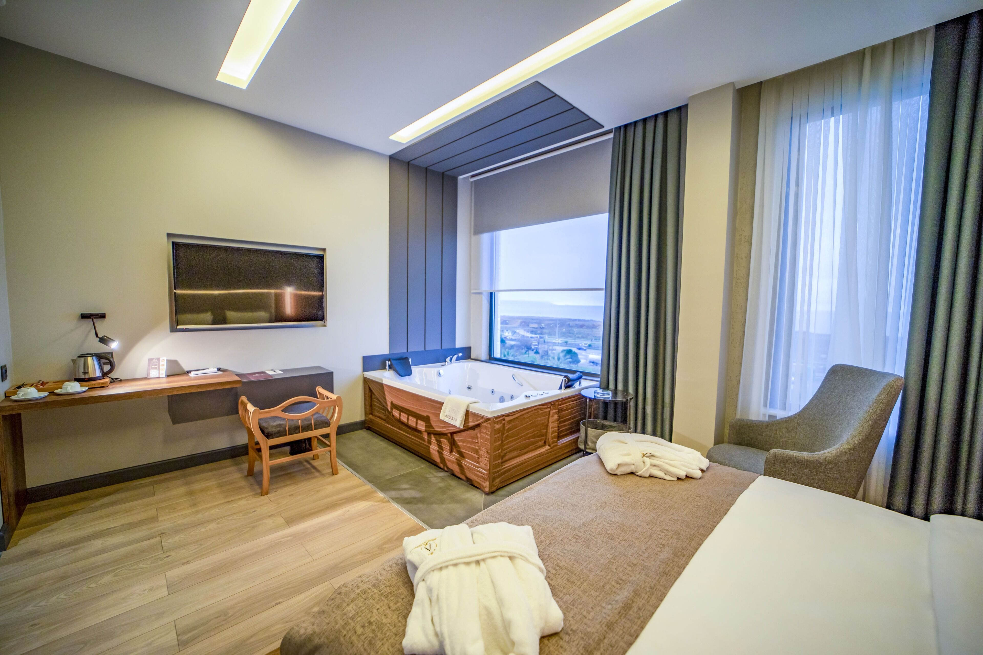 Una habitación de hotel moderna con una cama grande, una zona de estar con escritorio y silla, una bañera y vistas a la ciudad.