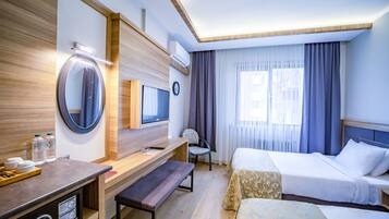 A hotel room with a wooden desk, a mirror, a television, a bed, and a window with curtains.