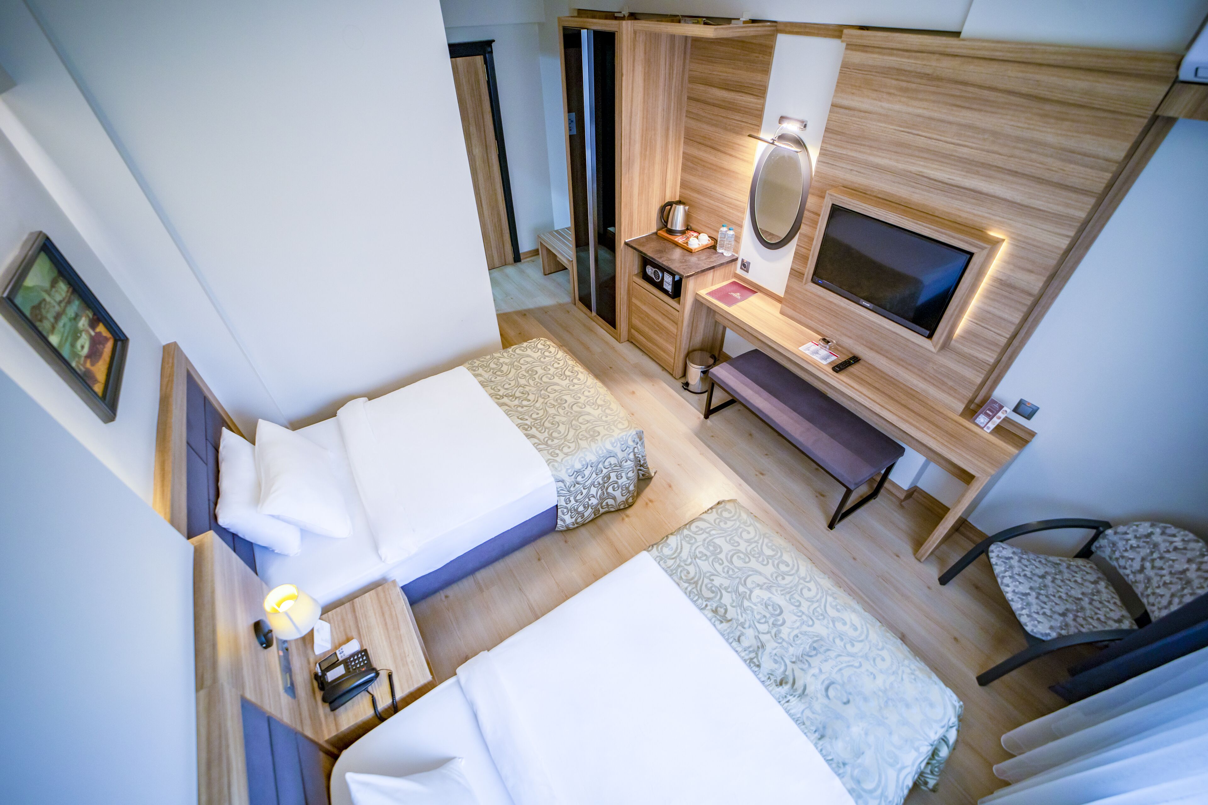 A compact hotel room with two single beds, a desk with a TV, a small seating area, and a bathroom with a shower and toilet.