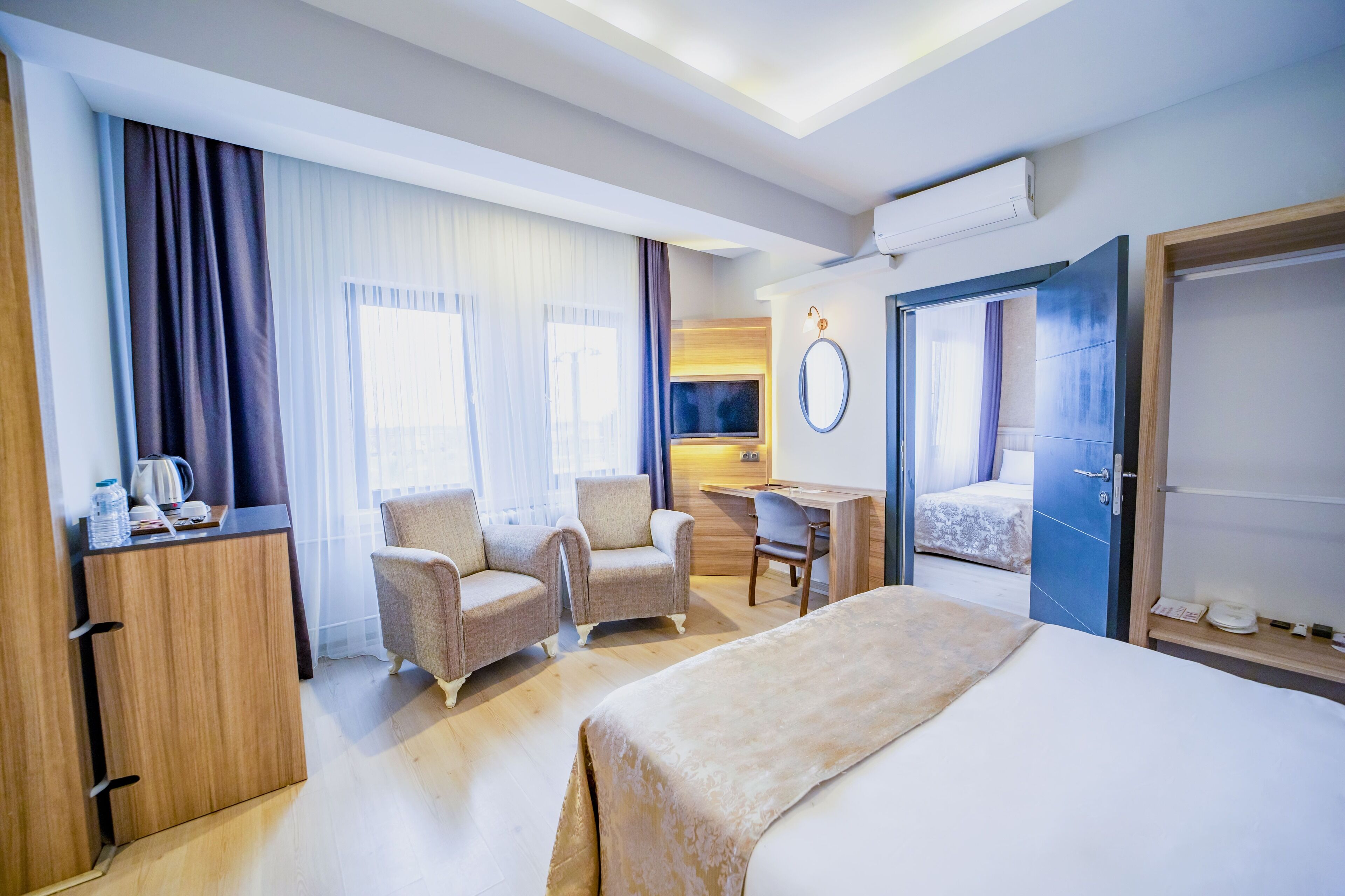 A hotel room with a bed, two armchairs, a desk, a wardrobe, and a mirror.