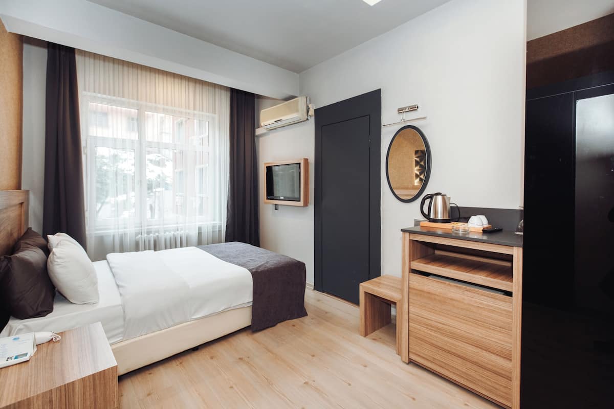 Ein modernes Hotelzimmer mit Bett, Nachttisch, Fernseher und einem kleinen Holzschrank.