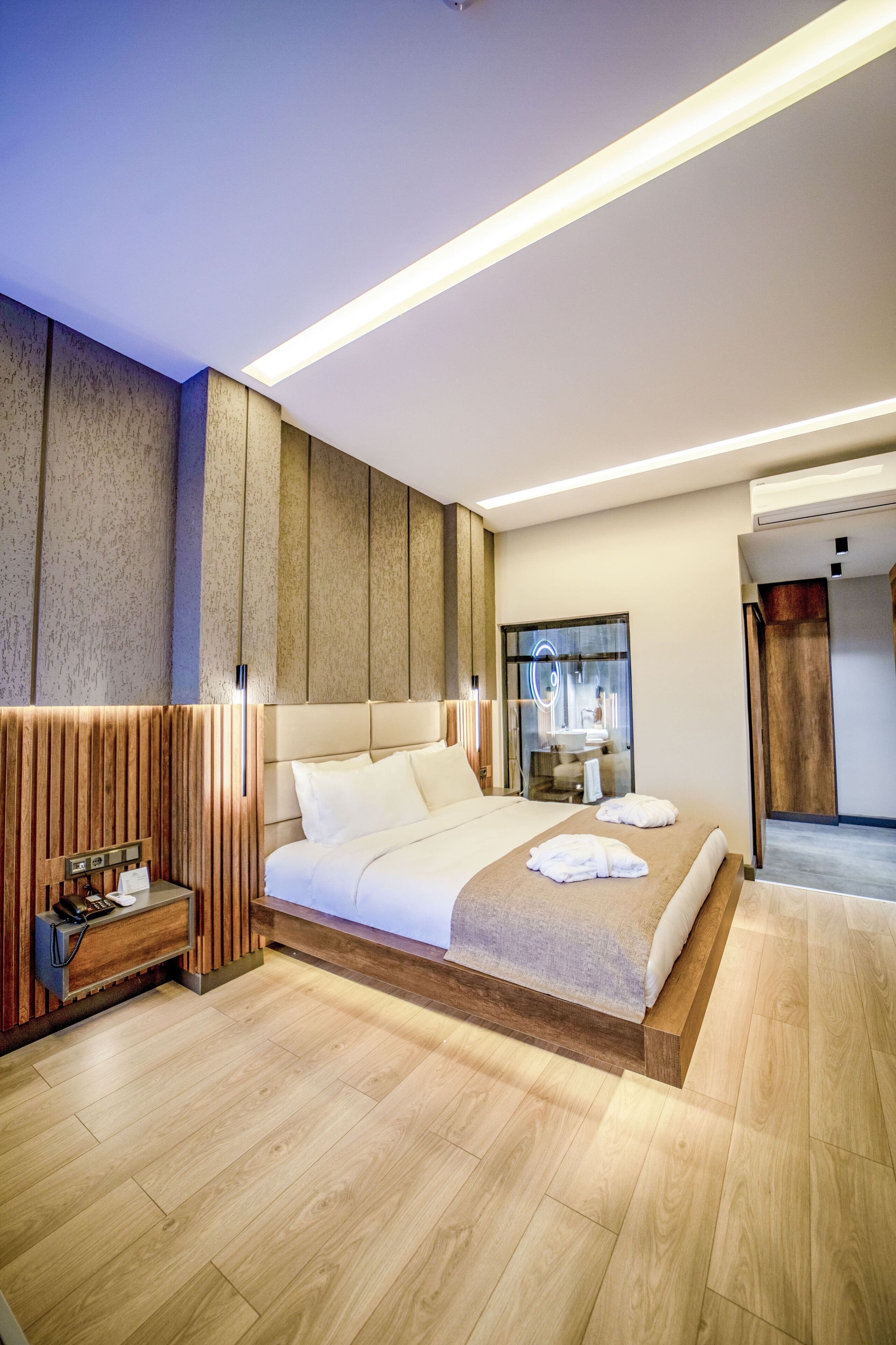 Ein modernes Hotelzimmer mit einem großen Bett, Holzvertäfelung und einem eingebauten Schreibtisch mit Telefon.