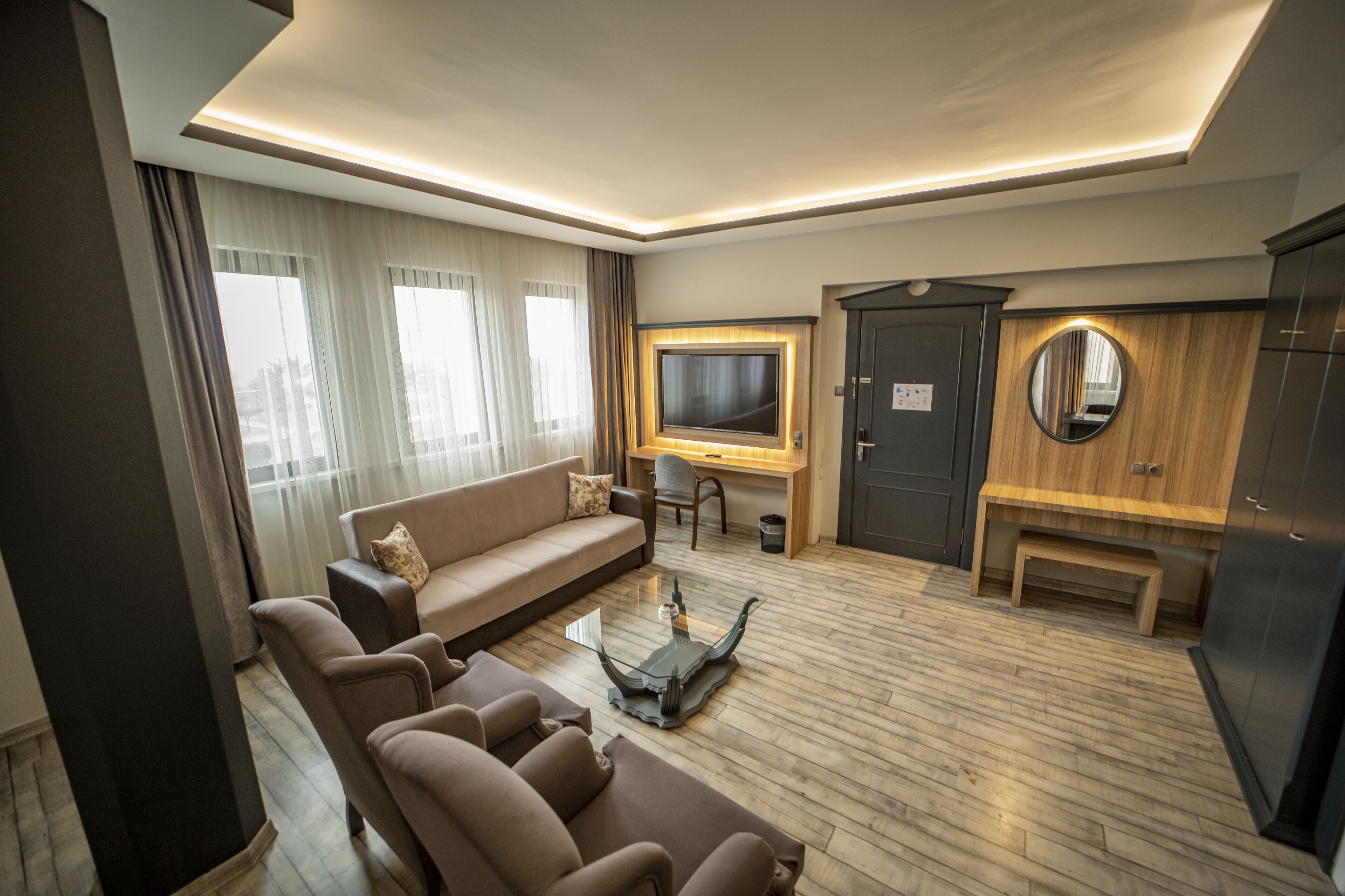 A modern living room with a sofa, armchairs, a coffee table, a TV, a wooden cabinet, and a mirror.