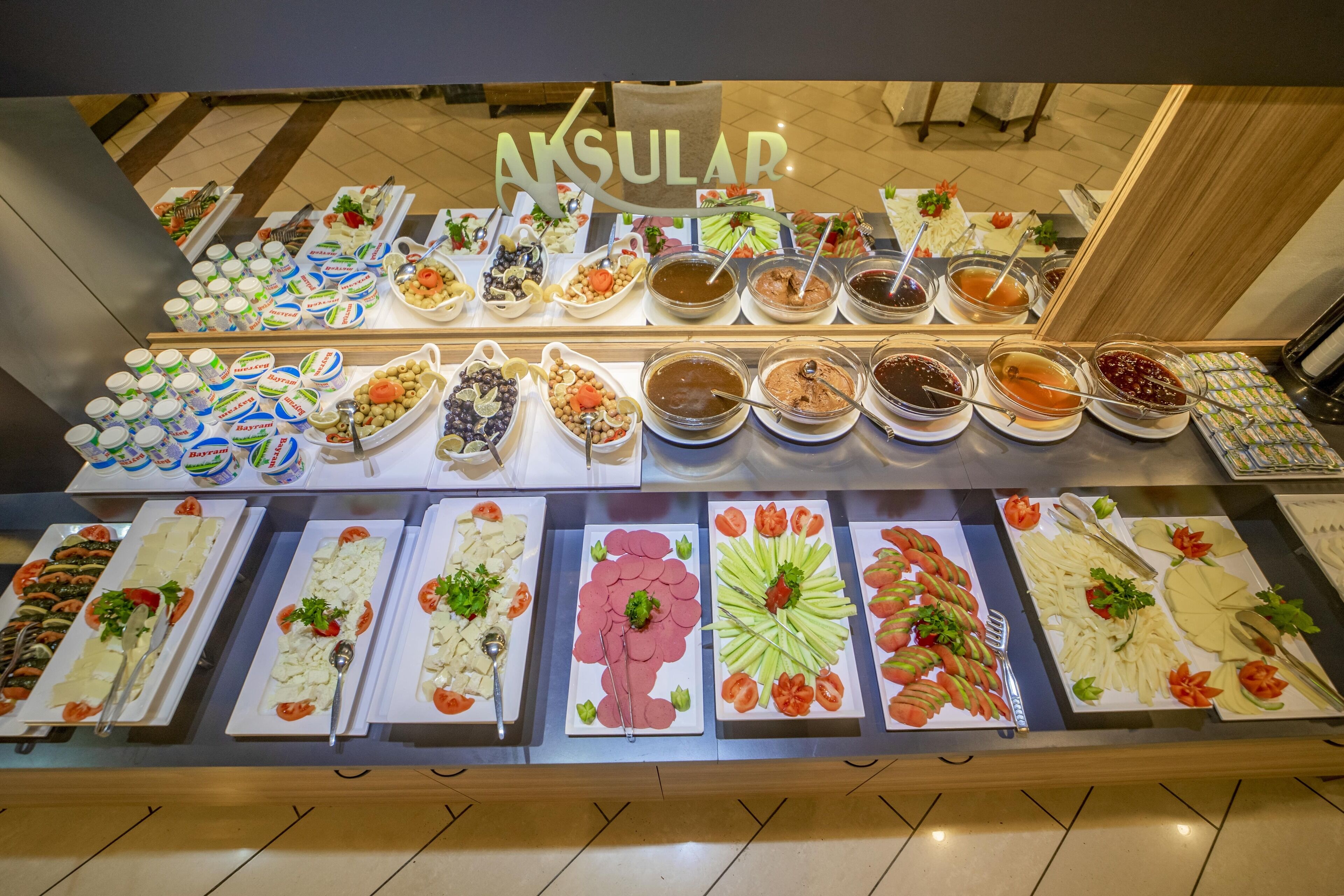 Un bufé con diversos alimentos, entre ellos ensaladas, carnes y salsas, dispuesto sobre una mesa.